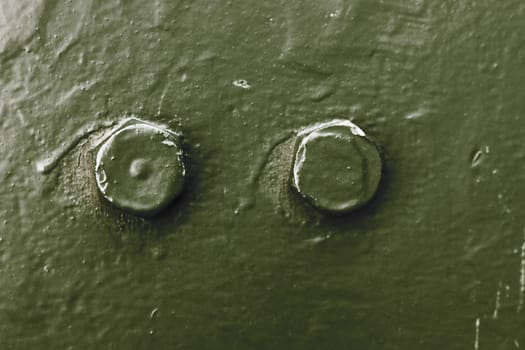 The metal surface of an armored vehicle with two bolts close-up, green.