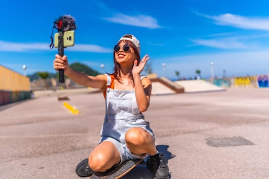 Asian young woman are doing livestreaming joyfully in skateboard urban park waving at the camera while recording