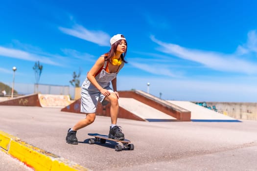 Full length photo of a cool asian young woman practicing in an urban skateboard park