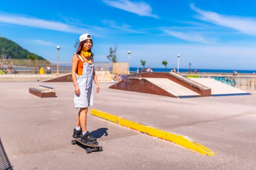 Young asian woman skateboarding in an urban park next to the sea in summer