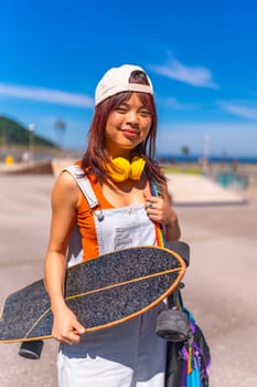 Vertical close-up portrait of a young asian skater in denim clothes and baseball cap in an urban park
