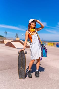 Asian woman holding a skateboard and adjusting her cap standing on a skateboard park