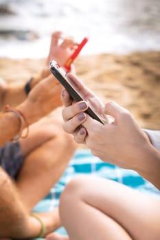 Man and woman hands typing on phone browsing social media phone sitting on beach