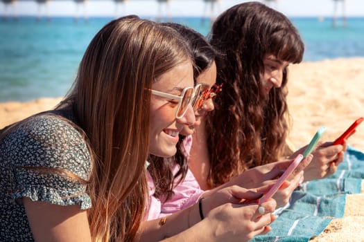 Group of smiling multiethnic women enjoying vacation. Beautiful and cheerful Gen Z girls with their mobile phones pose looking at the camera with a mobile phone.