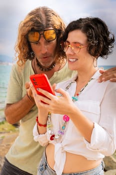 Middle aged man and woman sitting on the beach smiling browsing smartphone apps. Concept:Vacation and Technology