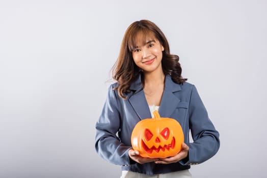 An enchanting studio portrait highlights the happiness of a young Asian female as she engages with an orange pumpkin, surrounded by whimsical ghost pumpkins on a white background. Halloween Day