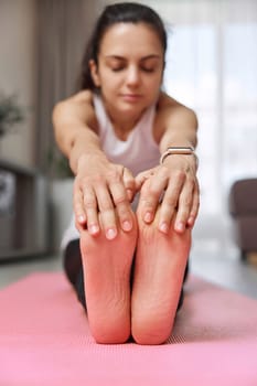 Sporty Caucasian woman worm up by stretching her body on pink exercise mat at home. focus on foot