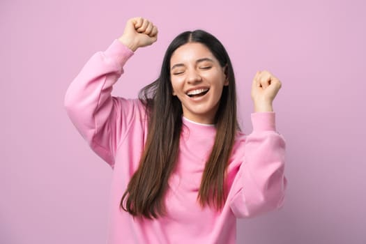Grooving in pink. Young woman blissfully dances with eyes shut, hands in the air, radiating joy and freedom.