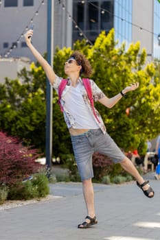 Young male tourist with backpack and sunglasses trying to catch a communication signal and Internet on mobile phone, raised the phone up for a better connection in city street. Frustrated guy in town.