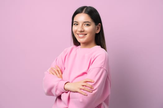 Serving looks and confidence. Young woman in a pink pullover, arms crossed and beaming. Pink backdrop for extra pop. Perfect for chic, modern, and empowered vibes.