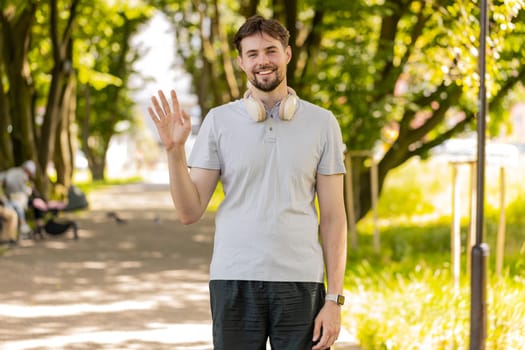 Hello, welcome. Athletic fit runner guy waving hi with palm greeting with hospitable friendly smile. Young Caucasian man jogger workout cardio training in park at morning. Active healthy sportsman.