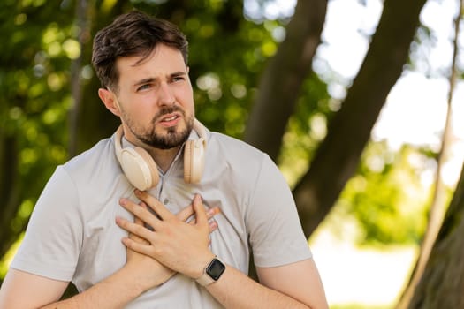Young adult sports man runner jogger having heart attack or chest pain after running workout in urban city park. A tired athlete suffers from tension in the heart. Health care and sports concept.