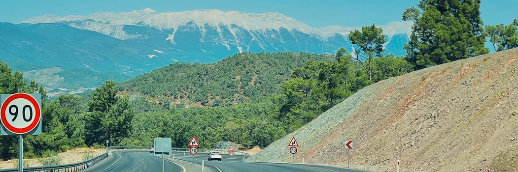 Banner of road among forests and mountains with a speed limit on sharp turns. soft focus.