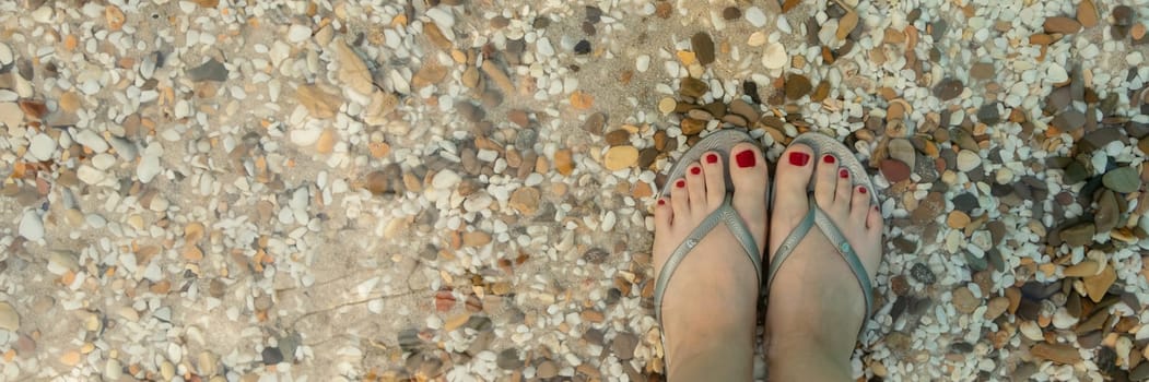 Concept banner for relaxing by the sea on a bright, hot and sunny day on the beach. top view of beautiful female legs with red pedicure on a background of sea pebbles. soft focus. Top view