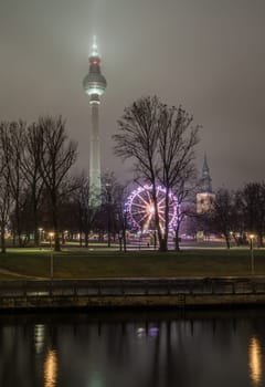 Berlin, Germany - Dec 19, 2023 - View of Famous Berlin Television Tower (Fernsehturm), Mary's Church Steeple and Ferris Wheel of Night Christmas Market near Alexanderplatz in Berlin, Copy space, Selective focus.