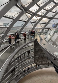 Berlin, Germany - Dec 20, 2023 - Several tourists walking at ramps inside the futuristic glass dome. A curved walkway stretches in spirals upwards on top inside the Reichstag building. Contemporary architecture of the Cupola of the Reichstag dome, a major tourist attraction of the berlin city, Copy space, Selective focus.