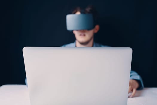 Person with VR headset using a laptop, immersed in virtual reality and modern technology experience.