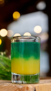 Alcoholic shot of green yellow color in bar at holiday party, close-up, vertical