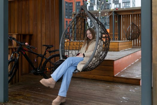 A woman is seated in a hanging chair on a porch, swinging gently back and forth as she enjoys the outdoor setting.