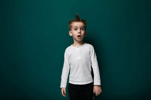 A young boy is standing in front of a vibrant green wall. He appears to be looking straight ahead, with a neutral expression on his face.