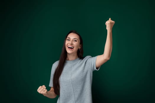 A woman wearing a grey shirt is standing and holding up a peace sign with her fingers. She is looking directly at the camera, with a neutral expression on her face.