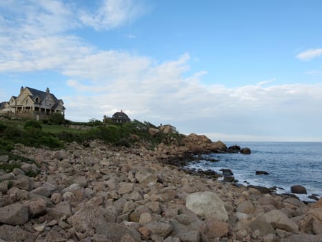 Gloucester - June, 6, 2014: A view of the rocky shoreline at Good Harbor Beach in Gloucester, Massachusetts, with a large house in the distance.