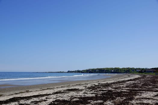 A wide shot of Scarborough Beach State Park in Maine, showcasing the sandy shoreline and clear blue sky.