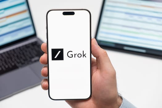 PRAGUE, CZECH REPUBLIC - JANUARY 21 2024: Grok logo on the screen of smartphone in mans hand on the workplace background.