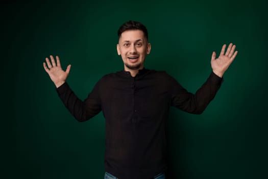 A man stands upright in front of a solid green background. He is wearing casual clothing and appears to be looking straight ahead. The background is a vibrant shade of green with no discernible features.