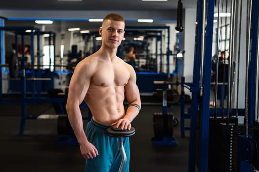 Portrait of muscular bodybuilder holding a barbell standing in the fitness center.