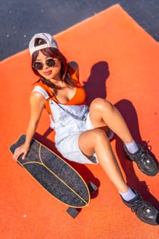 Vertical top view portrait of a confident chinese woman sitting next to skateboard in a colorful urban park