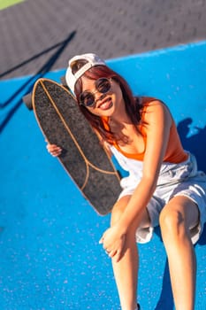 Vertical top view portrait of a happy skater with modern clothes and sunglasses sitting on blue colorful park smiling at camera