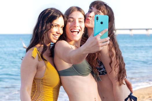 Group of smiling multiethnic women in swimsuits enjoying vacation. Beautiful and cheerful girls of generation Z pose for a photo with a mobile phone.