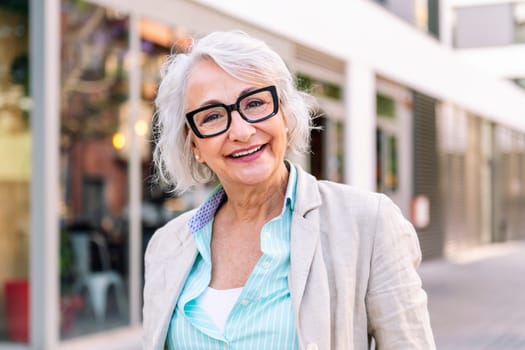 portrait of a stylish mature woman smiling happy looking at camera outdoors, concept of urban lifestyle in adulthood