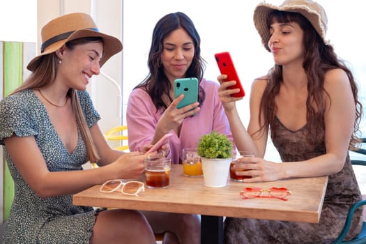 Group of smiling multiethnic women enjoying vacation in a restaurant. Beautiful and cheerful Generation Z girls browsing the internet with smartphones