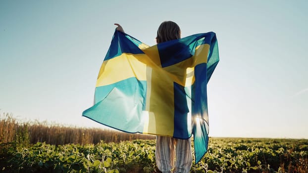 Unrecognizable swedish little kid - patriot child boy jumps with national flag on sky sunset background at summer. Sverige celebration banner, holidays in Sweden. High quality