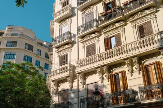 Two historic buildings with ornate balconies and intricate facades. The architectural details and lush greenery create a picturesque and charming urban scene.