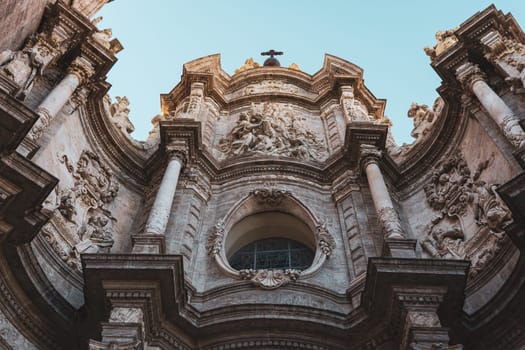 Upward view of the ornate facade of Valencia Cathedral with intricate carvings and architectural details. The historical structure stands against a clear sky, showcasing its grandeur.