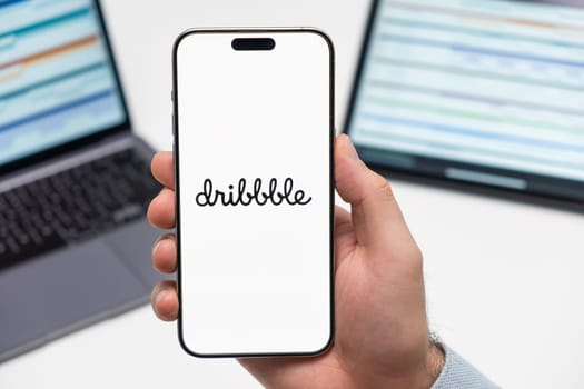 PRAGUE, CZECH REPUBLIC - JANUARY 21 2024: Dribbble logo on the screen of smartphone in mans hand on the workplace background.