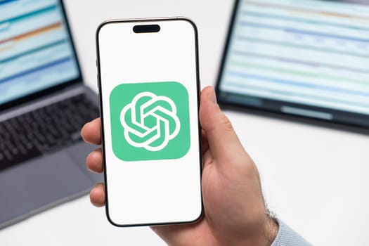 PRAGUE, CZECH REPUBLIC - JANUARY 21 2024: ChatGPT Open AI logo on the screen of smartphone in mans hand on the workplace background.