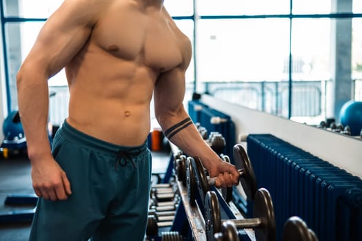 Muscular man in a white t-shirt works out in the gym with dumbbells. Biceps pumping. Fitness and bodybuilding concept. Mixed media. High quality photo