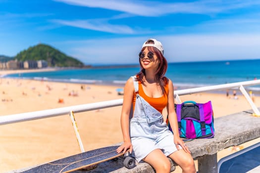 Horizontal photo with copy space of an asian young woman sitting on a promenade with skateboard in summer