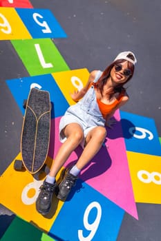 Vertical top view of a chinese young woman with skate sitting above a colorful graffiti in a park