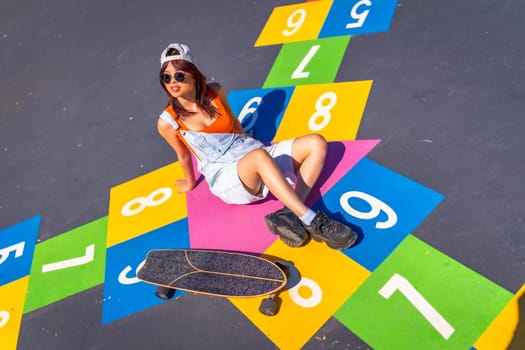 Cool young female chinese skater sitting above a colorful picture of street art in an urban skateboard park
