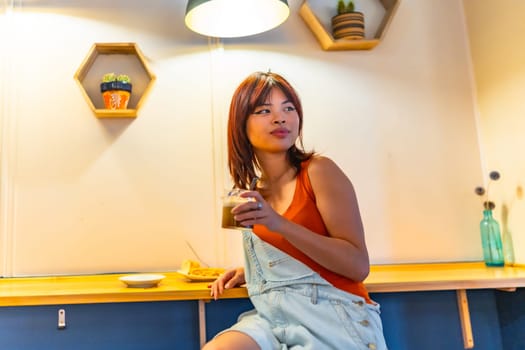 Low angle view portrait of a cute casual and young asian woman drinking coffee in a modern cafeteria