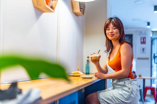 Portrait with copy space of a smiling asian youthful woman drinking coffee in a cafeteria