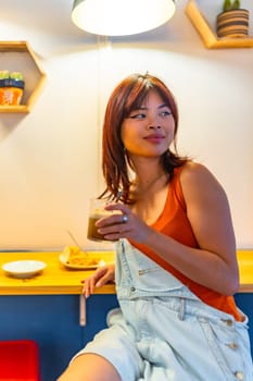 Vertical portrait of an asian beauty young distracted woman enjoying coffee in a modern cafeteria