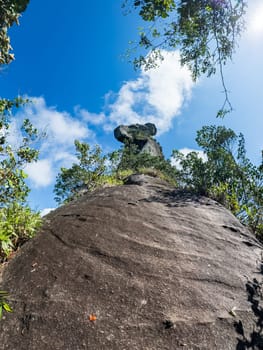 A tall Papagayo rock stands against a clear blue sky with sunlight peeking through.