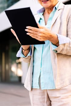 unrecognizable mature woman smiling happy while using digital tablet outdoors in the city, concept of urban lifestyle in adulthood and technology o communication