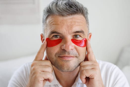 a man applies moisturizing patches with vitamins under his eyes, a modern cosmetic product for the eyes to smooth out fine wrinkles and remove redness